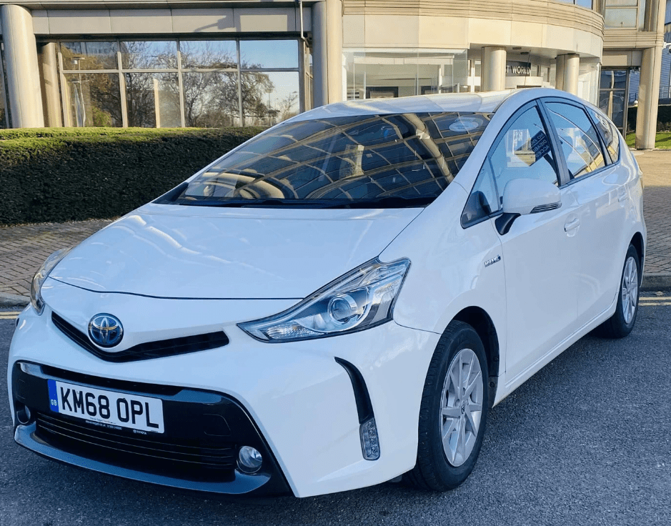 a white Toyota Prius plus parked in the shade outside a building