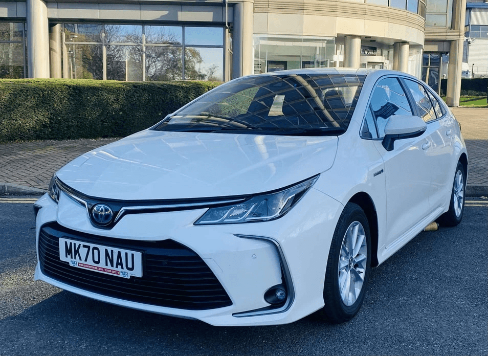 a white Toyota corolla PCO car for rent in London parked in the shade at the curb outside a building