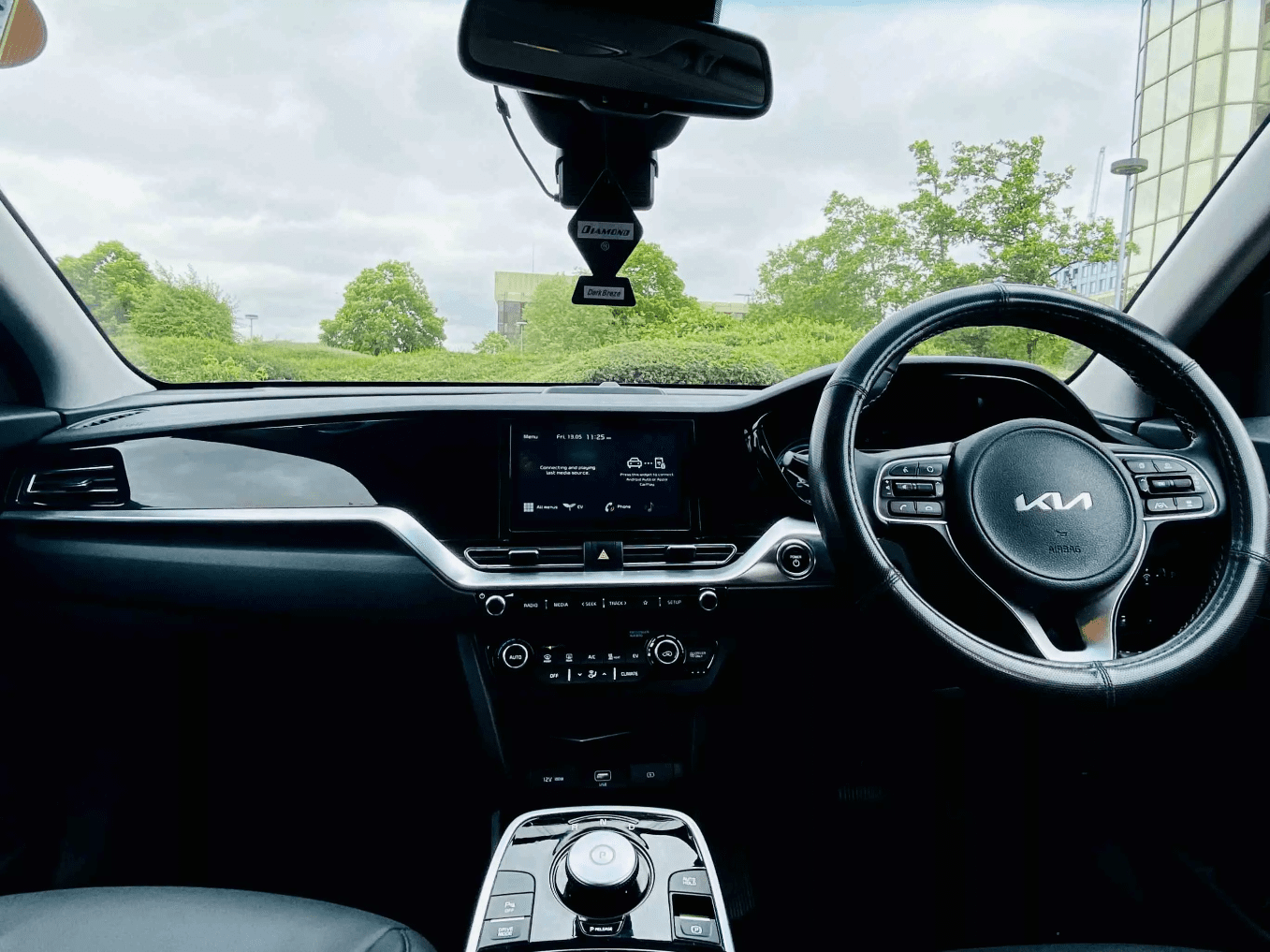 the interior of a Kia E-Niro PCO car for hire with a view of trees and a garden visible from the windscreen